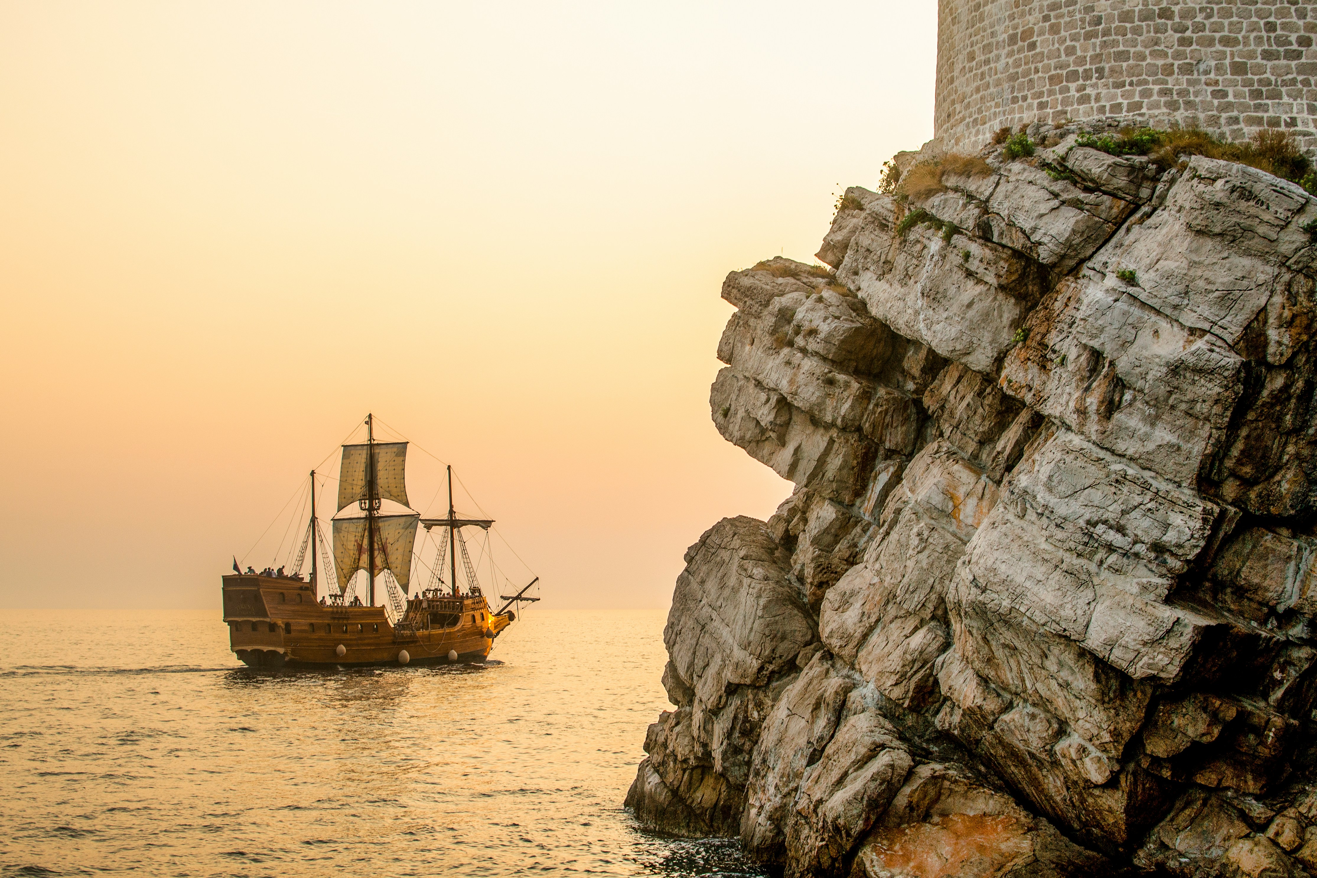 Lanscape with cliffs in the foreground, the sea and a traditional large ship sailing across the horizon