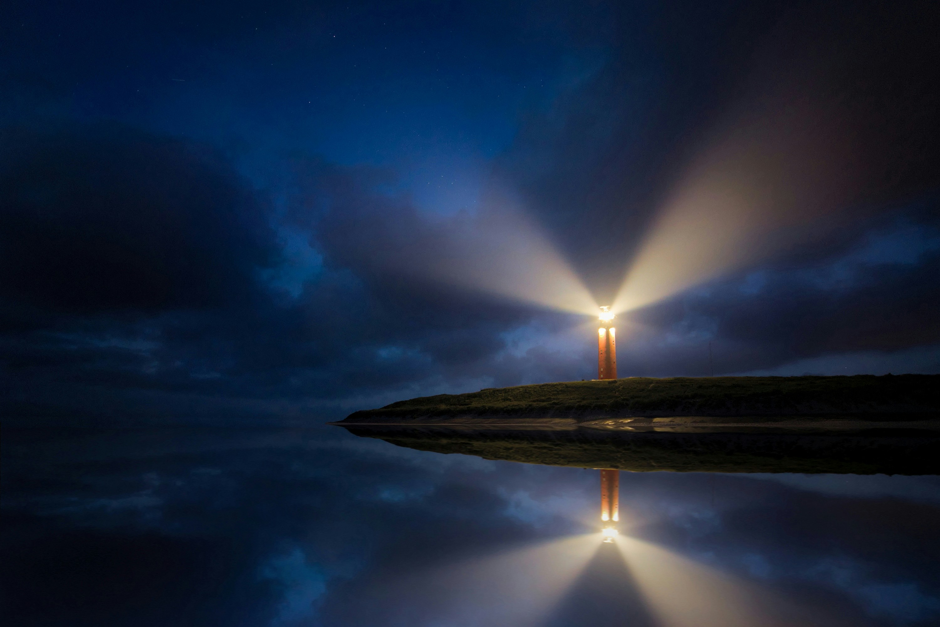 A lighthouse shining out into the night in a peninsula surrounded by blue-coloured Sea